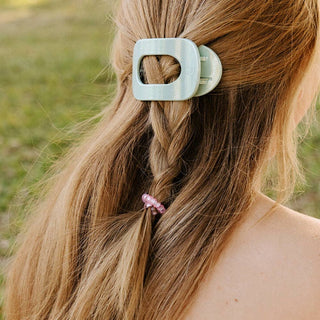 Woman wearing sage green hair clip with blonde hair in braid secured by pink spiral hair coil.