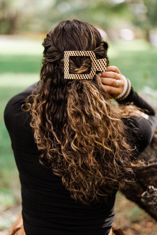 Woman wearing checkered square flat hair clip in long curly brown hair outdoors