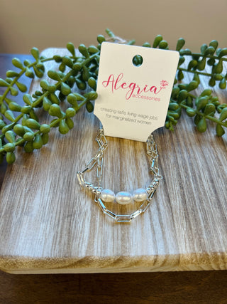 Silver chain bracelet with pearls displayed on wooden surface with succulent plants and brand tag.