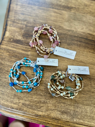 Three Simply Noelle beaded stretch bracelets with natural stones displayed on a wooden surface.
