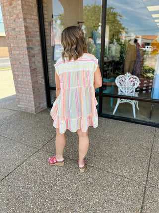 Woman wearing colorful striped sleeveless top with ruffle hem, standing on outdoor patio