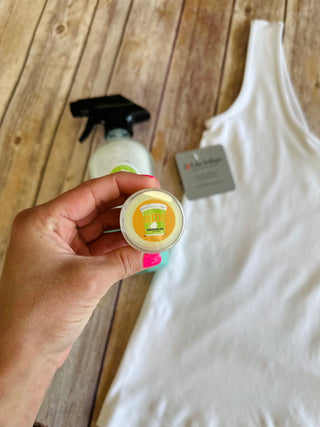 Hand holding small round container of SUDS stain remover with white clothing and spray bottle visible.