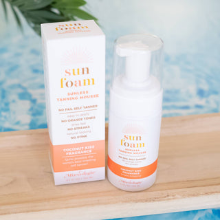 SunFoam sunless tanning mousse bottle and packaging displayed on wooden surface with tropical background