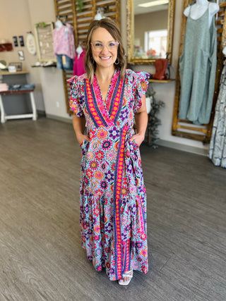 Woman wearing colorful patterned wrap dress with floral and geometric prints in clothing boutique setting.
