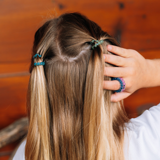 Person styling long hair with TELETIES tiny hair ties, holding extra coils on fingers.