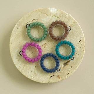 Five coiled spiral hair ties arranged on a round stone display dish by TELETIES.