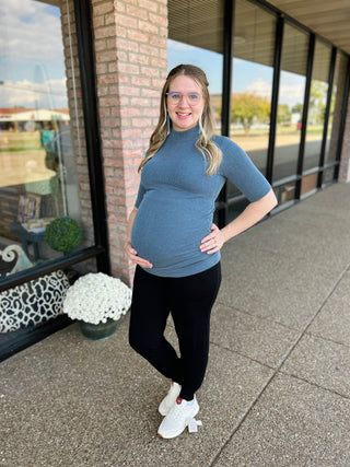 Pregnant woman wearing blue ribbed mock neck maternity top with black leggings and white sneakers