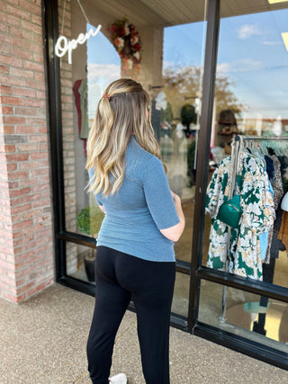 Woman wearing blue ribbed mock neck top standing outside clothing boutique storefront