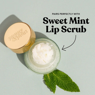 Open jar of Sweet Mint Lip Scrub with gold lid and fresh mint leaves on white background.