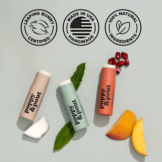 Three Poppy & Pout lip balms with certification badges, mint leaves, fruit slices, and pomegranate seeds.