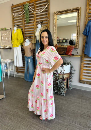 Woman wearing floral striped maxi dress in boutique setting with mirrors and clothing displays