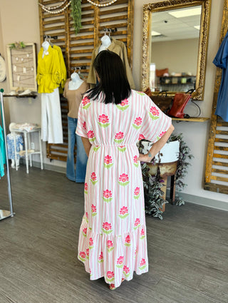 Woman wearing pink striped floral maxi dress with ruffled hem in boutique setting with mirror