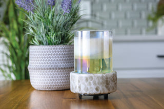 Swirled glass candle warmer with iridescent finish on wooden surface next to potted lavender plant