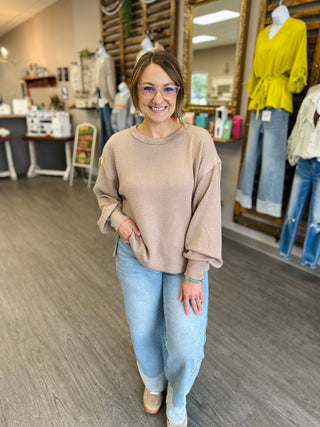 Woman wearing a relaxed-fit textured crew neck pullover top with long sleeves in a boutique.