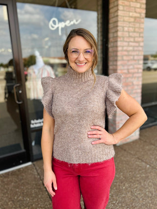 Woman wearing a turtleneck ruffle sleeve knit sweater paired with red pants outside a boutique.