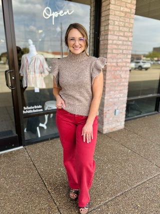 Woman wearing a sleeveless turtleneck sweater with ruffle cap sleeves outside a boutique storefront.
