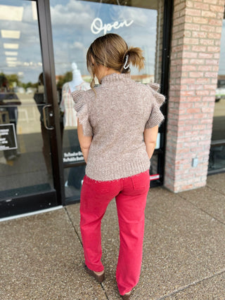 Woman wearing a short-sleeve ruffle shoulder knit sweater with mock neck, rear view.