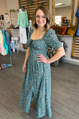 Woman wearing floral maxi dress with square neckline and puffed sleeves in clothing boutique