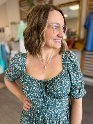 Woman smiling in teal floral maxi dress with lace-up front and puffed sleeves
