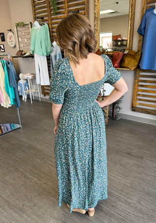 Woman wearing floral maxi dress with smocked bodice and short sleeves in boutique setting