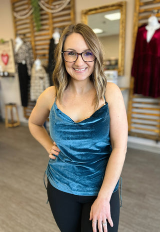 Woman wearing blue velvet tank top in clothing boutique with clothing displays in background.