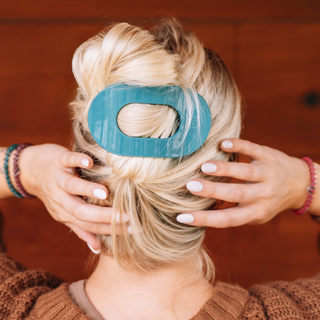 A woman wearing a large oval hair clip securing a twisted updo hairstyle, viewed from behind.