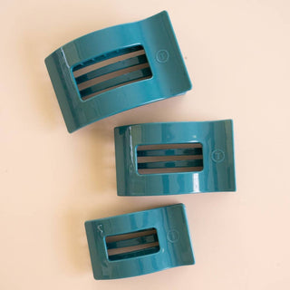 Three TELETIES flat rectangle hair clips in glossy teal, arranged in varying sizes on a neutral background.