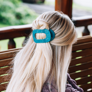 Person with blonde hair wearing a TELETIES flat round hair clip in a half-up style outdoors.