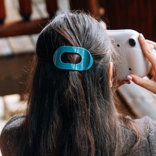 Woman wearing a TELETIES flat round hair clip in a half-up hairstyle, holding a camera.