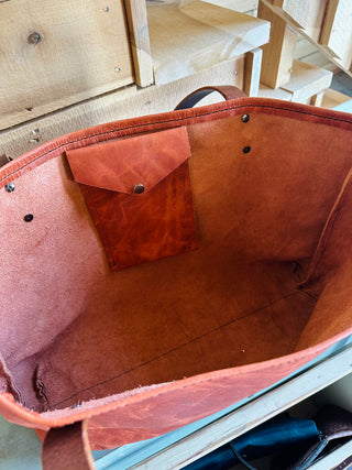 Open brown leather weekender tote bag showing interior compartment and pocket detail on wooden surface.