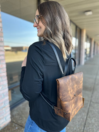 Woman wearing brown leather backpack while walking through covered walkway, showing side profile view.