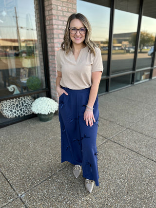 Woman wearing navy blue wide-leg pants with bow details and beige top, standing outside modern building.