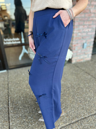 Woman wearing blue wide-leg pants with decorative bow details and side pockets, styled with casual top.