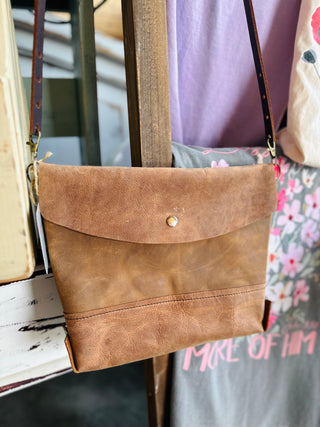 Brown leather crossbody bag with flap closure and adjustable strap displayed on wooden rack