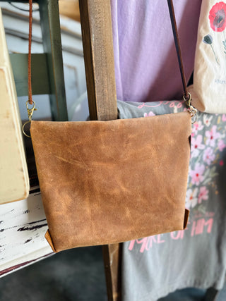 Brown leather crossbody bag with adjustable strap displayed among other handbags in boutique setting.
