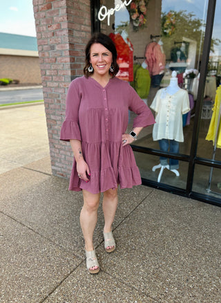 Woman wearing a button-front tiered dress with bell sleeves standing outside a clothing boutique.