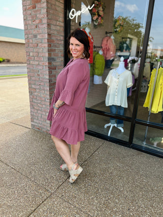 Woman wearing pink tiered dress with ruffles standing outside boutique storefront