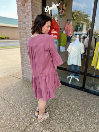 Woman wearing pink tiered ruffle dress with bell sleeves standing outside clothing boutique storefront.