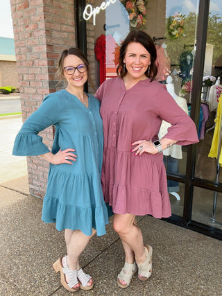 Two women wearing tiered button-front dresses with bell sleeves standing outside clothing store entrance