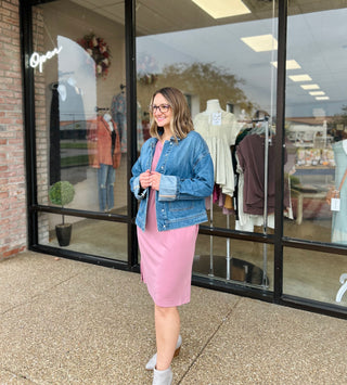 Woman wearing denim cargo snap jacket over pink dress standing outside clothing boutique storefront