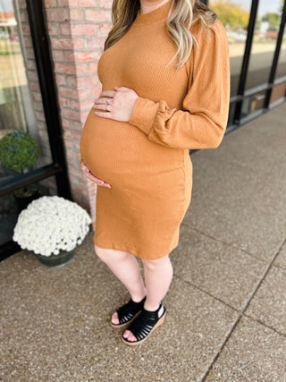 Pregnant woman wearing ribbed knit maternity dress with long sleeves, cradling belly outdoors