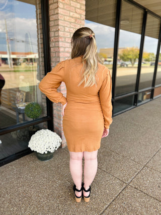 Woman wearing orange ribbed knit dress with long sleeves, standing outside storefront with hand on hip.