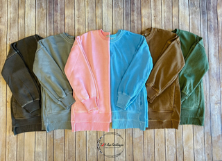 Five colorful pullover sweatshirts laid flat on wooden background displaying different color options available.