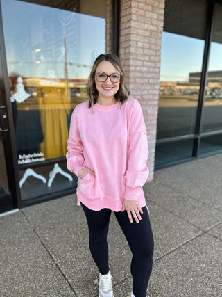Woman wearing pink oversized pullover sweatshirt with black leggings and white sneakers, smiling outdoors.