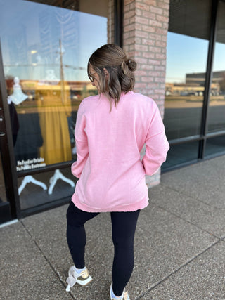 Woman wearing pink pullover sweatshirt and dark leggings walking past storefront windows