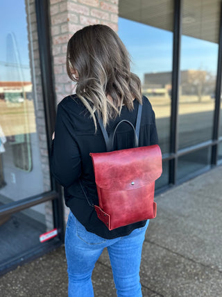 Woman wearing red leather backpack with black top and jeans, standing outside storefront.