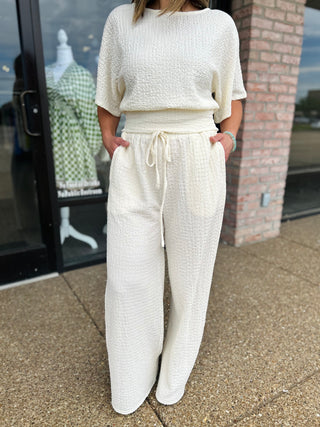 Woman wearing Allie Rose Gathered Grace wide-leg textured drawstring pants with matching top outdoors.