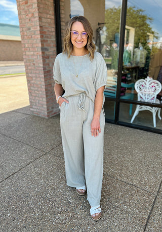 Woman wearing casual ribbed matching top and pants set with white sandals standing outdoors.