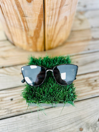 Stylish sunglasses with dark lenses and metal frames displayed on artificial grass against wooden background.