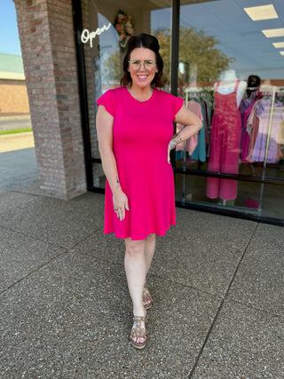 Woman wearing bright pink flutter sleeve dress standing outside boutique storefront
